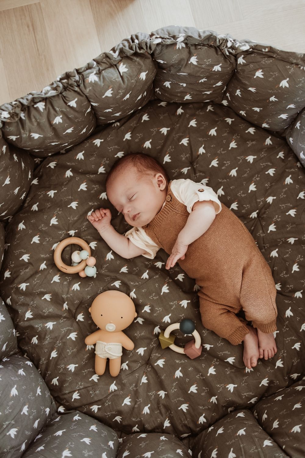 bloom birds babymat, crib, raised edges, little baby is sleeping in the crib, wooden toys and doll