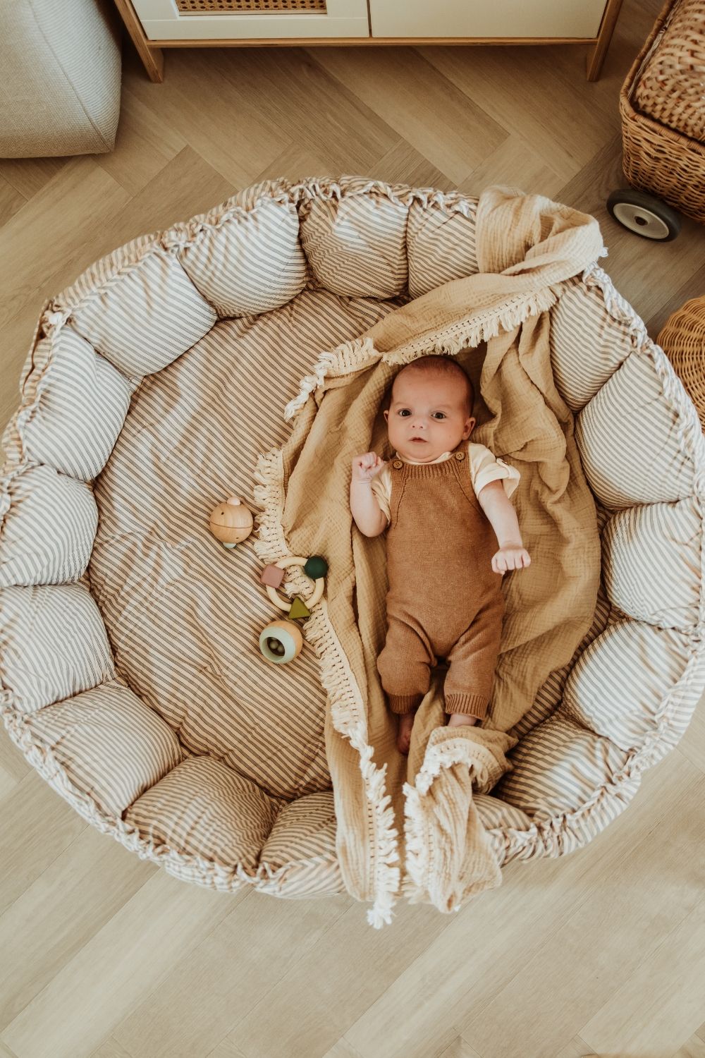 bloom stripes blue babymat, crib, raised edges, baby is lying on a blanket in the crib, wooden toys