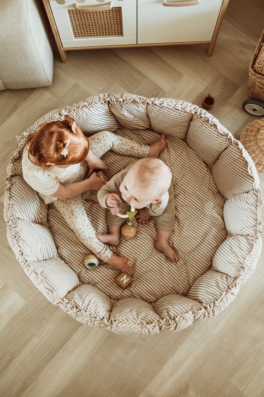 bloom stripes blue babymat, crib, raised edges, baby and toddler are sitting and playing in the crib
