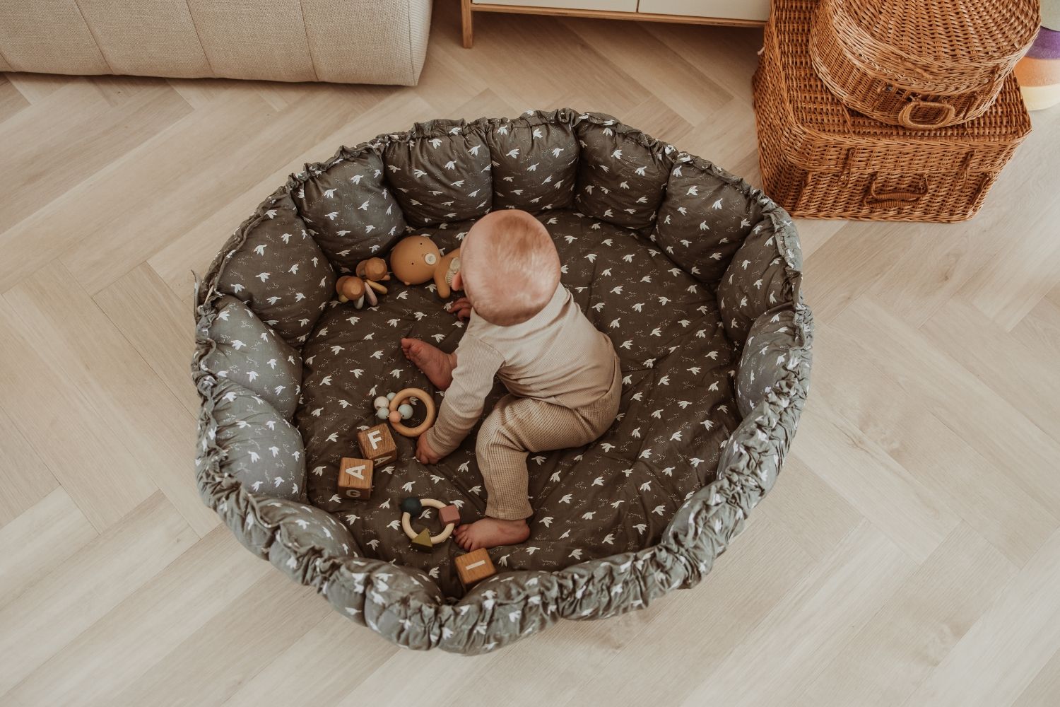 bloom birds babymat, crib, raised edges, child is sitting in the crib, wooden toys and a doll