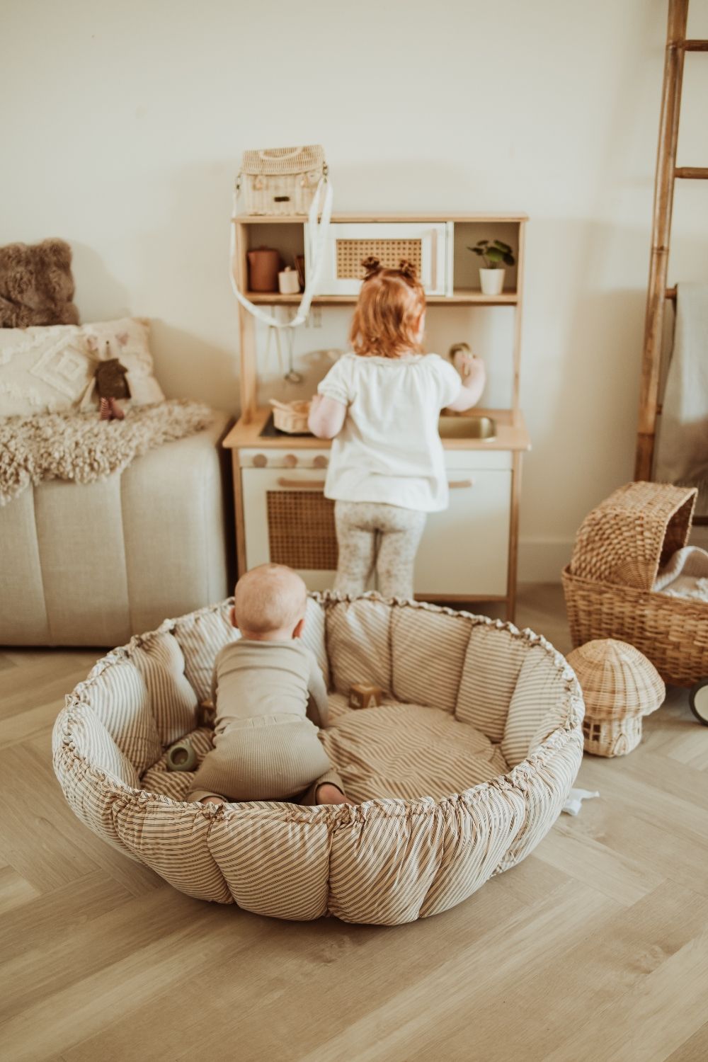 bloom stripes blue babymat, crib, raised edges, baby is in the crib, looking at toddler who is playing with wooden kitchen