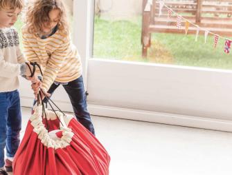 two siblings closing a red storage bag.