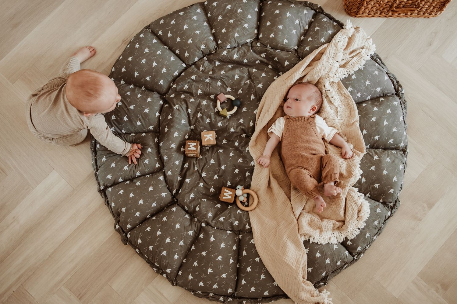 bloom birds babymat, open on floor, baby is lying on the mat on a blanket, other child is crowling towards lying baby, wooden toys