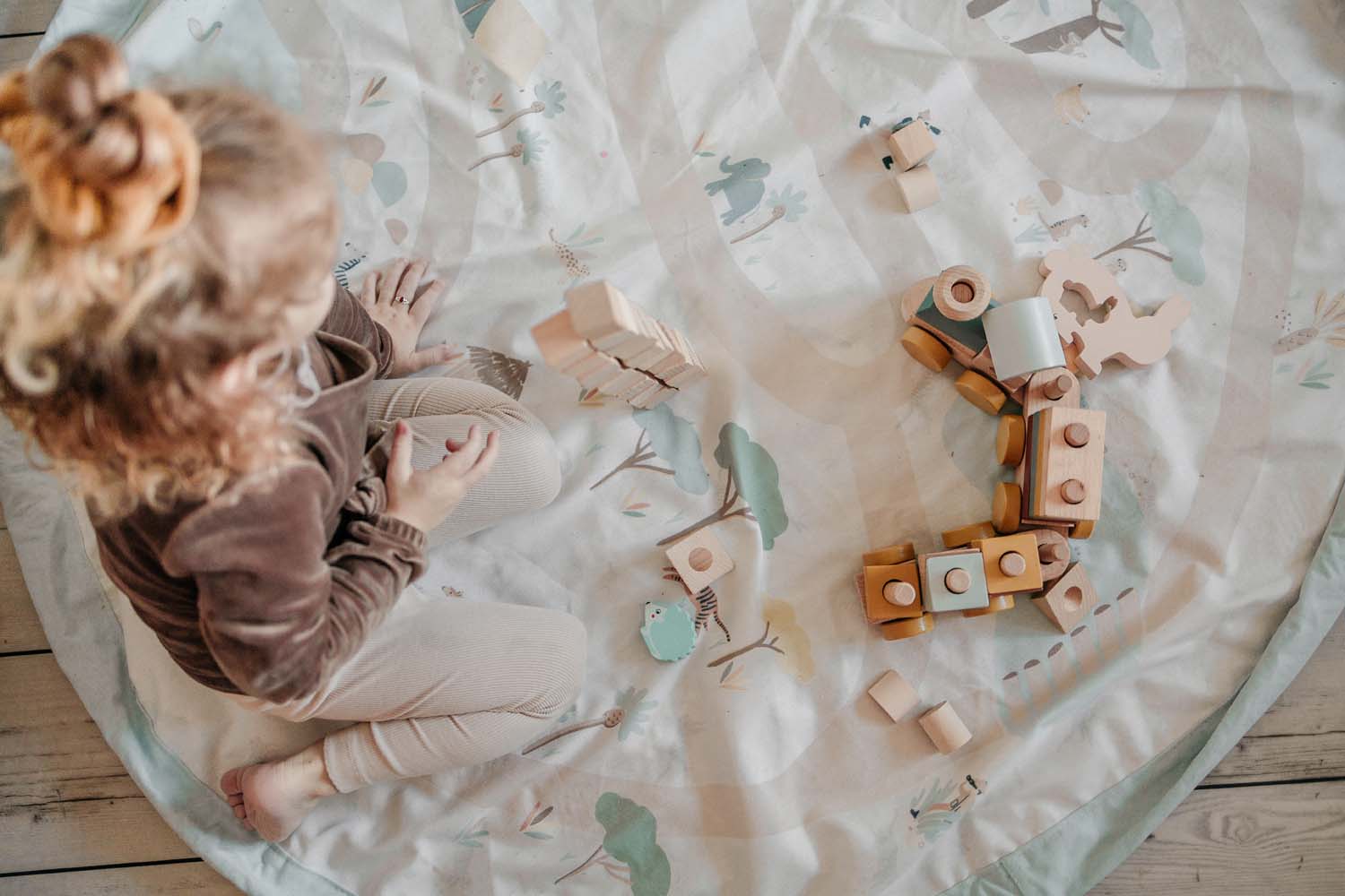 jungle storage bag, child playing on open mat on floor, wooden train