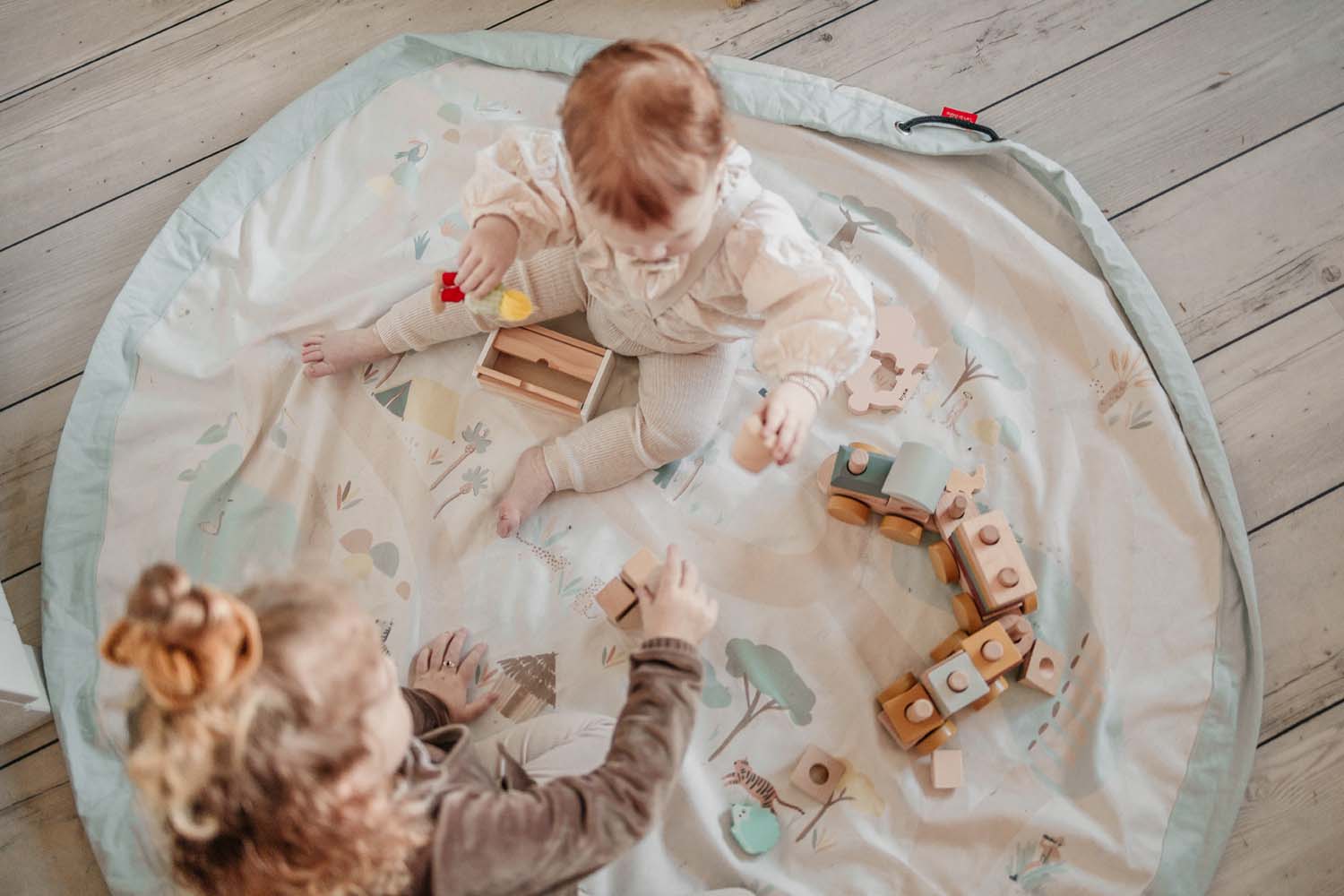 jungle storage bag, children playing on open mat on floor, wooden train and wooden toys