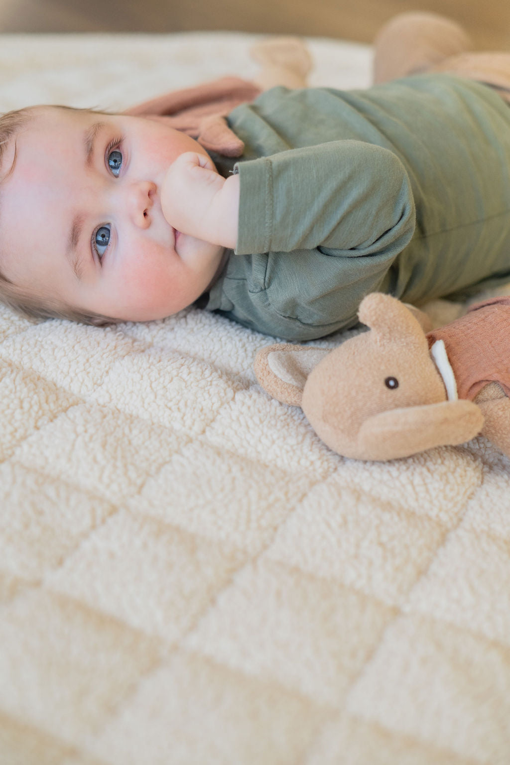 noomad soft teddy oak, baby is lying on the mat with cuddle, awake