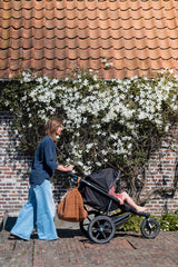noomad soft teddy brown, person is pushing a stroller with child inside, closed bag is hanging on the stroller