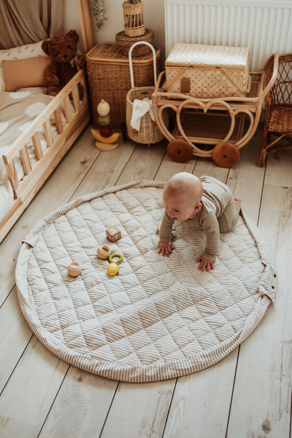 soft stripes blue organic babymat, baby is crowling over the open mat on floor in kidsroom, wooden toys and baskets