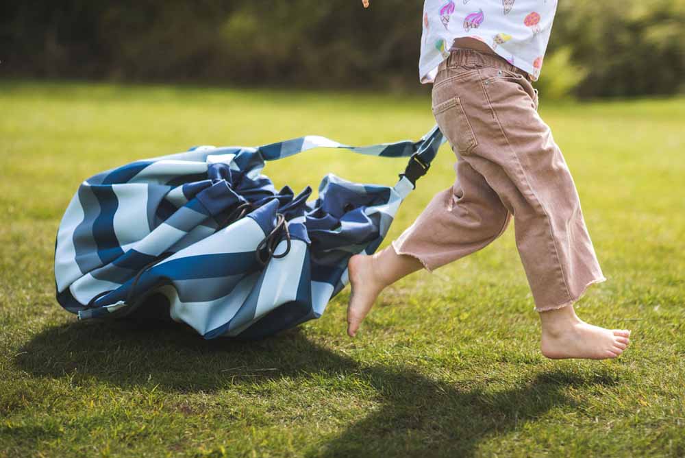 outdoor storage bag blue/green stripes, child running in garden pulling closed bag 