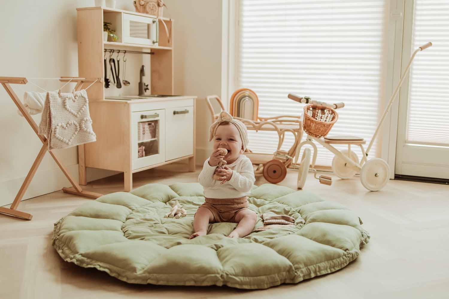 Bloom meadow green organic babymat, child sitting on open mat on floor in kidsroom, laughing and playing, wooden kitchen, tricycle