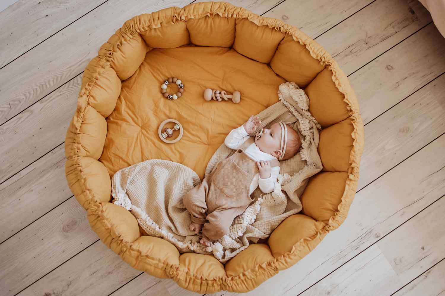 Bloom mustard organic babymat, raised edges, little baby lying on the mat, on little blanket