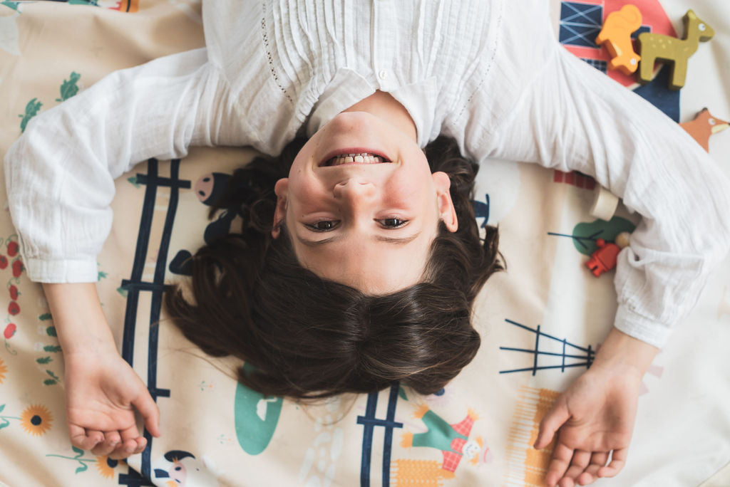 farm storage bag and play mat, laughing child lying on mat, between wooden toys